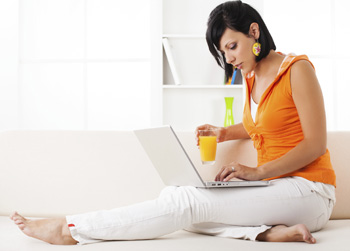 Frau arbeitet in gemütlicher Position auf der Couch am Laptop.